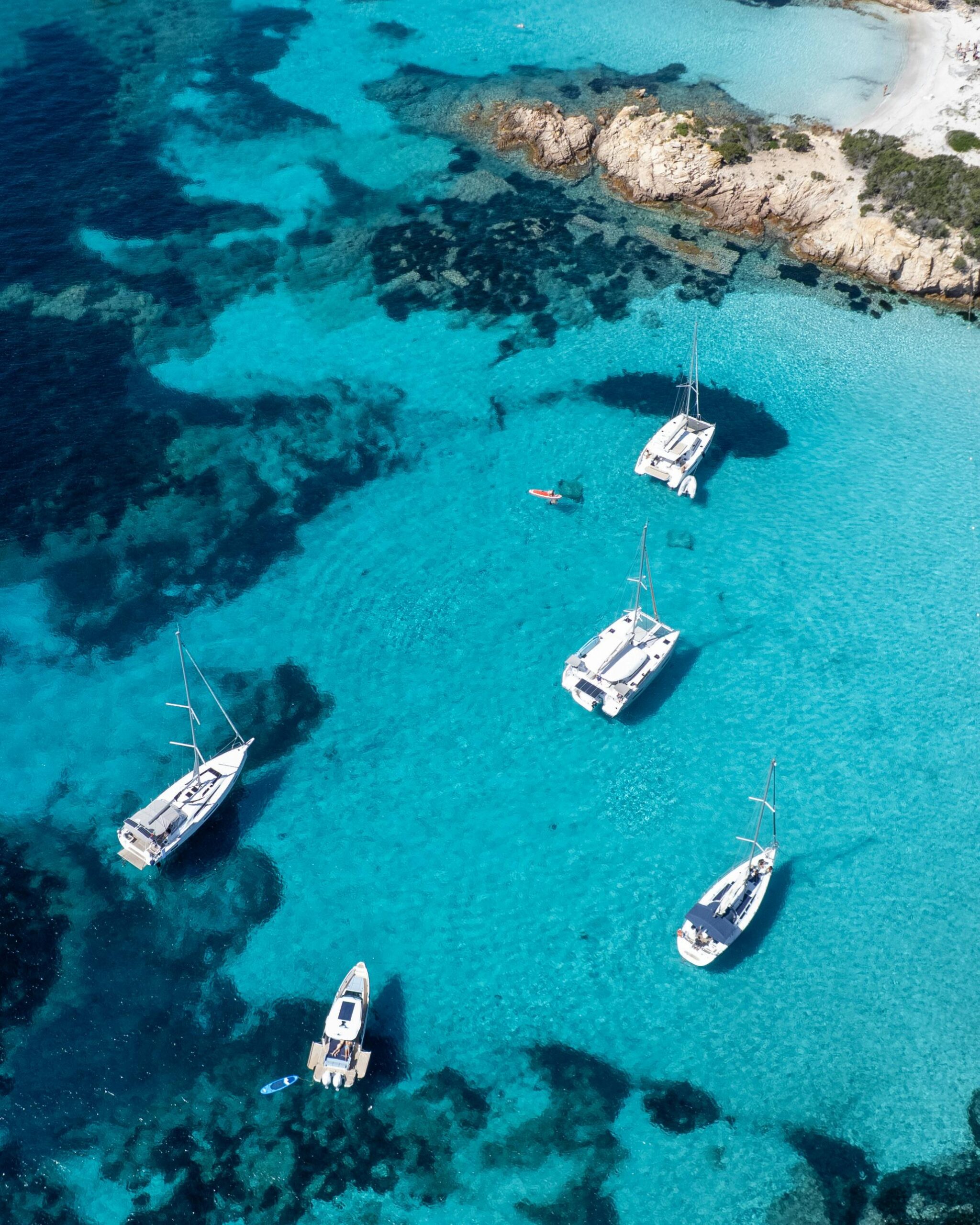 A breathtaking aerial view of sailboats in turquoise seas near a rocky coastline.